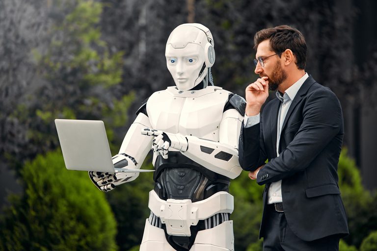 Humanoid AI robot laptopot használ egy gondolkodó üzletember mellett. Az AI ügynökök vállalati használatát szemléltető kép.